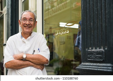 senior hispanic barber in old fashion barber's shop, posing and looking at camera with arms crossed near shop window - Powered by Shutterstock