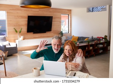 Senior Hispanic Couple At Home With Laptop Having Video Chat With Family