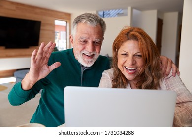 Senior Hispanic Couple At Home With Laptop Having Video Chat With Family