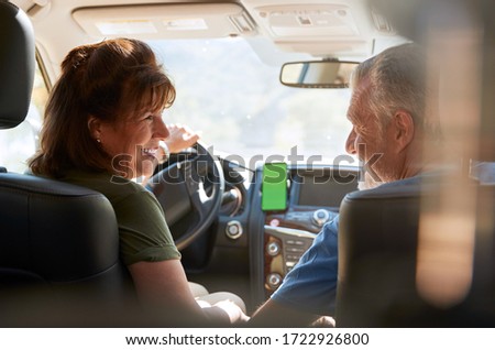 Senior Hispanic Couple On Drive Through Countryside Using Sat Nav On Mobile Phone