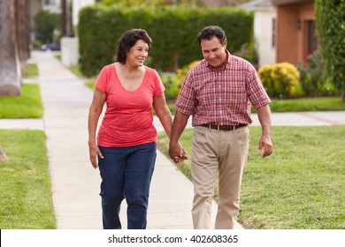 Senior Hispanic Couple Walking Along Sidewalk Together