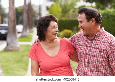 Senior Hispanic Couple Walking Along Sidewalk Together