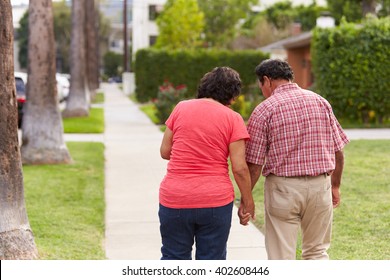 Senior Hispanic Couple Walking Along Sidewalk Together