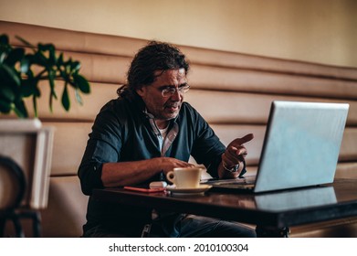 Senior hispanic cuban men using laptop for an online meeting with his colleagues while remote working in a cafe