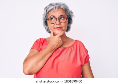 Senior hispanic grey- haired woman wearing casual clothes and glasses with hand on chin thinking about question, pensive expression. smiling with thoughtful face. doubt concept.  - Powered by Shutterstock