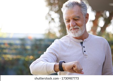 Senior Hispanic Man Checking Health Monitor On Smart Watch In Garden At Home