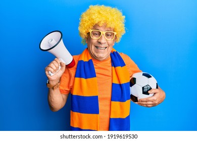 Senior hispanic man football hooligan cheering game holding ball and megaphone smiling and laughing hard out loud because funny crazy joke. 