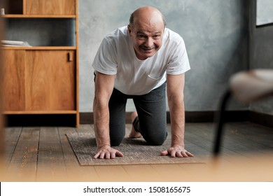 Senior Hispanic Man Practices Yoga Asana Marjariasana Or Cat-cow Pose At Home. Doing Sport Exercise For Spine Health.