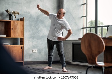 Senior Hispanic Man Practicing Yoga Trikonasana Pose At The Living Room