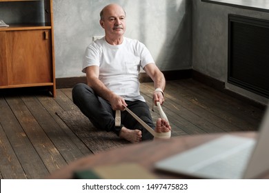 Senior Hispanic Man Sitting In Janushirshasana Seated Forward Bend Posture, Exercise For Hips And Spine At Home Using Belt.