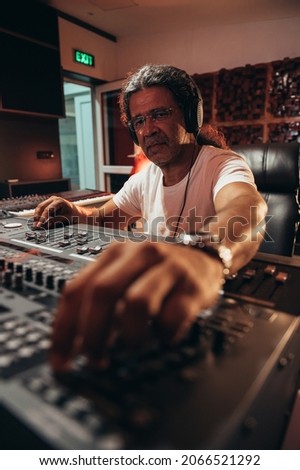 Senior hispanic music producer working on a mixing soundboard while in his studio