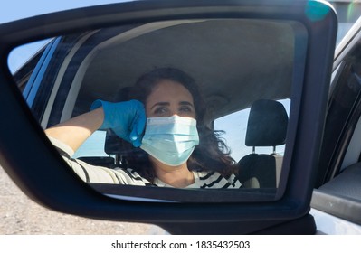 Una anciana hispana con máscara facial y guantes de látex conduciendo su auto visto desde el espejo retrovisor del auto. Concepto de Covid-19 (virus Corona).