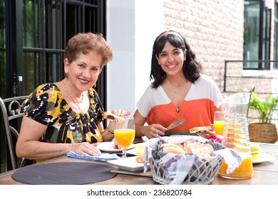 A Senior Hispanic Woman Having Breakfast Outdoors With A Daughter. Outdoor Dining In Summer. Focus On Senior Woman.