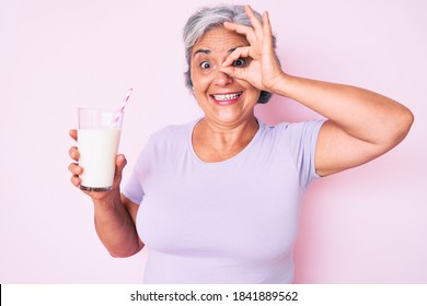 Senior Hispanic Woman Holding Glass Of Milk Smiling Happy Doing Ok Sign With Hand On Eye Looking Through Fingers 