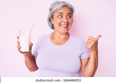 Senior Hispanic Woman Holding Glass Of Milk Pointing Thumb Up To The Side Smiling Happy With Open Mouth 