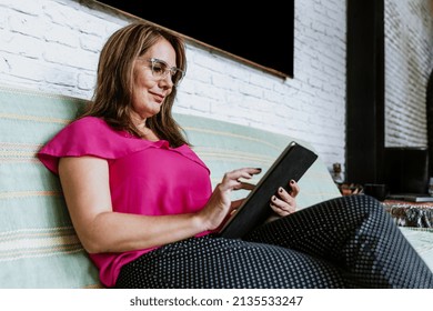 Senior Hispanic Woman Middle Age Working At Home In Sofa With Digital Tablet Or Home Office In Mexico Latin America
