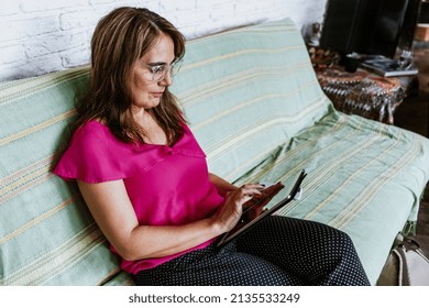 Senior Hispanic Woman Middle Age Working At Home In Sofa With Digital Tablet Or Home Office In Mexico Latin America
