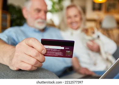 Senior holding a debit card to pay for online shopping on the computer at home on the sofa - Powered by Shutterstock