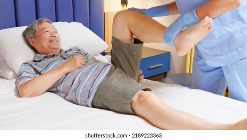 Senior Home Health Care Concept - Asian Female Physiotherapist Is Helping Senior Elder Man Lying On Bed Stretching His Hamstring And Doing Thigh Or Leg Rehabilitation