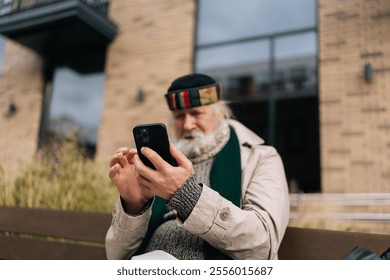 Senior homeless man sitting on urban bench, using smartphone, checking messages or browsing internet, highlighting intersection of technology and homelessness in modern society. - Powered by Shutterstock