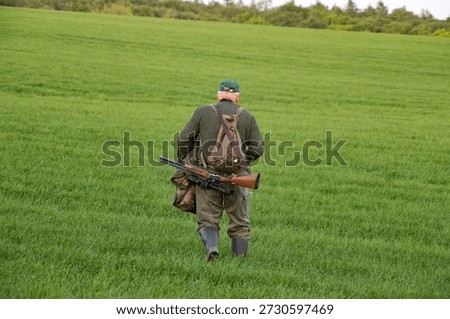 Senior hunter with backpack walking through green grass at dusk