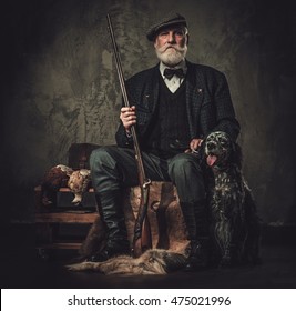 Senior hunter with a english setter and shotgun in a traditional shooting clothing on a dark background.
