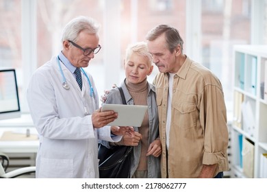 Senior husband embracing ill wife and supporting her while doctor showing test results on tablet - Powered by Shutterstock