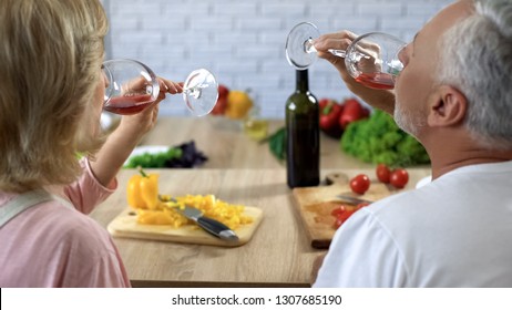 Senior husband and wife drinking red wine home, cooking salad for dinner, date - Powered by Shutterstock