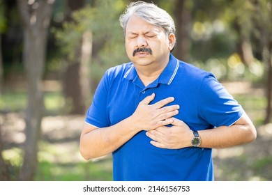 Senior Indian asian male presses hand to his chest as he is suffering from bad pain or heart attack at park outdoor, old people heart disease problem, healthcare concept.