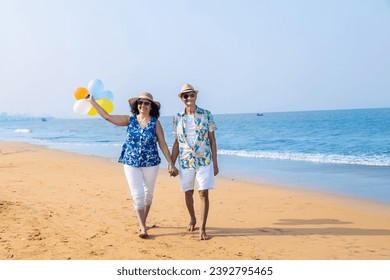 Senior indian couple with colorful balloon in hands walking together at the beach. Enjoying vacation, holiday at beach. Copy space. - Powered by Shutterstock