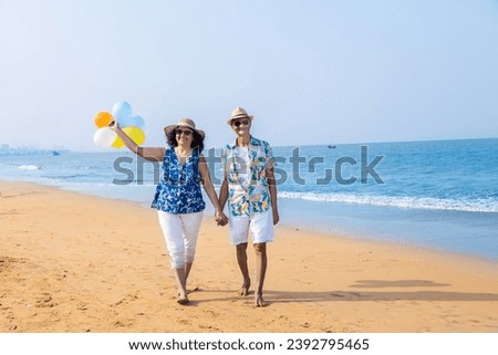 Senior indian couple with colorful balloon in hands walking together at the beach. Enjoying vacation, holiday at beach. Copy space.