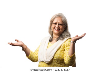 Senior Indian Lady In Punjabi Dress With Eye Glasses, With Hands Folded Or Presenting Something With Copy Space, Standing Isolated Over White