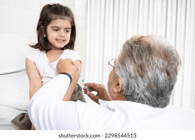 Senior Indian man pediatrician performs a vaccination of a little girl. Doctor administering an injection to a female child in a clinic. Injecting syringe needle in shoulder. - Powered by Shutterstock