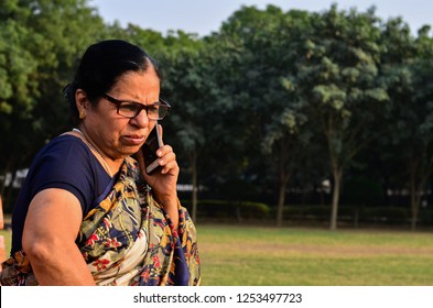 Senior Indian woman giving angry expressions speaking on her smartphone, sitting on a bench in a park in Delhi. Concept shot showcasing technology adoption by senior citizens. Digital India