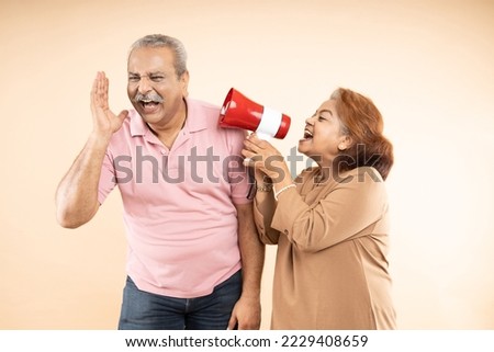 Senior indian woman scream or shouting at man in megaphone isolated on beige background. announce discounts sale. Asian wife tease husband. Mental peace. Hurry up. referral