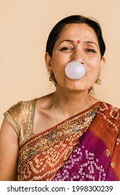 Senior Indian Woman In A Traditional Saree Blowing A Bubble With A Chewing Gum