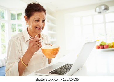 Senior Indian Woman Using Laptop Whilst Eating Breakfast