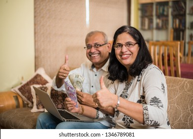 Senior Indian/asian couple accounting, doing home finance and checking bills with laptop, calculator and money while sitting on sofa/couch at home