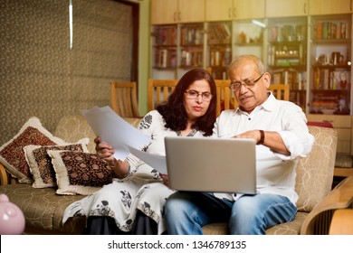 Senior Indian/asian Couple Accounting, Doing Home Finance And Checking Bills With Laptop, Calculator And Money While Sitting On Sofa/couch At Home