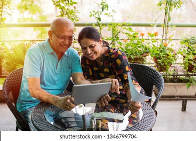 Senior Indian/asian Couple Accounting, Doing Home Finance And Checking Bills With Laptop, Calculator And Money While Sitting On Sofa/couch Or Dining Table At Home