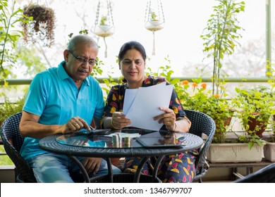 Senior Indian/asian couple accounting, doing home finance and checking bills with laptop, calculator and money while sitting on sofa/couch or dining table at home