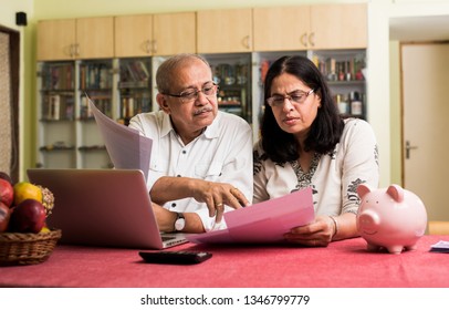 Senior Indian/asian couple accounting, doing home finance and checking bills with laptop, calculator and money while sitting on sofa/couch or dining table at home