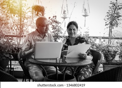 Senior Indian/asian Couple Accounting, Doing Home Finance And Checking Bills With Laptop, Calculator And Money While Sitting At Home Garden