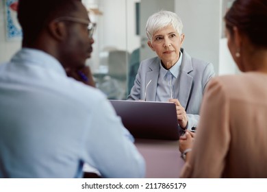 Senior insurance agent using laptop while talking toa couple during the meeting in her office. - Shutterstock ID 2117865179