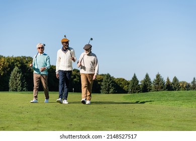 senior interracial friends walking with golf clubs on green field - Powered by Shutterstock