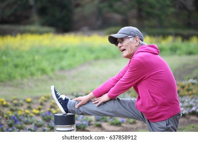 Senior Japanese Man Wearing Pink Parka Doing Standing Hamstring Stretch