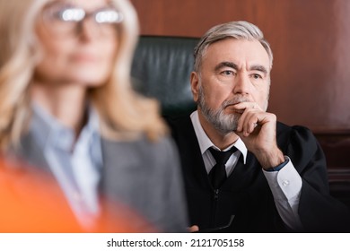 Senior Judge Holding Hand Near Face While Thinking Near Advocate On Blurred Foreground