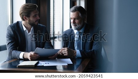 Senior and junior businessman discuss something during their meeting, office background.