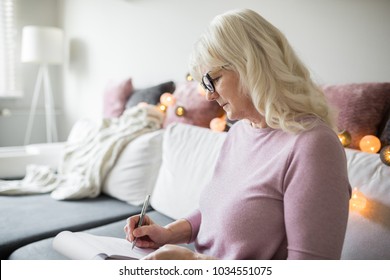 Senior Lady In Glasses Taking Notes At Home