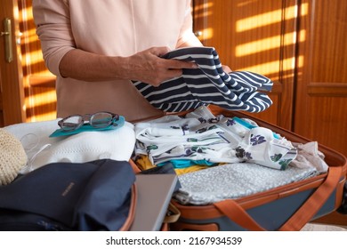 Senior Lady Packing Her Stuff Into A Suitcase Preparing For Summer Vacation Trip. Elderly Woman Checking Accessories In Luggage On The Bed At Home Before Travel. Traveling Preparation Concept